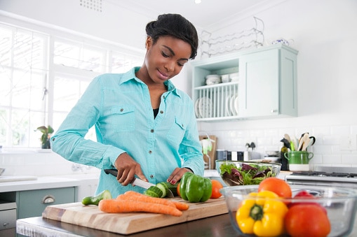 African female in the kitchen chopping a cucumber for her lunch that she's busy preparing. Cape Town, Western Cape, South Africa.