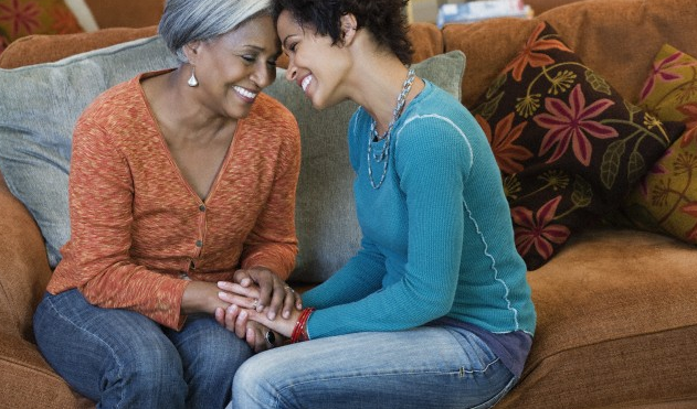 An older mother and her adult daughter touching their heads together and smiling