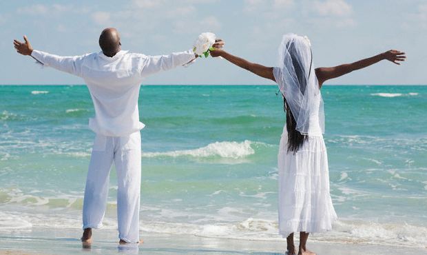 A bride and groom extended their arms out in front of a beach