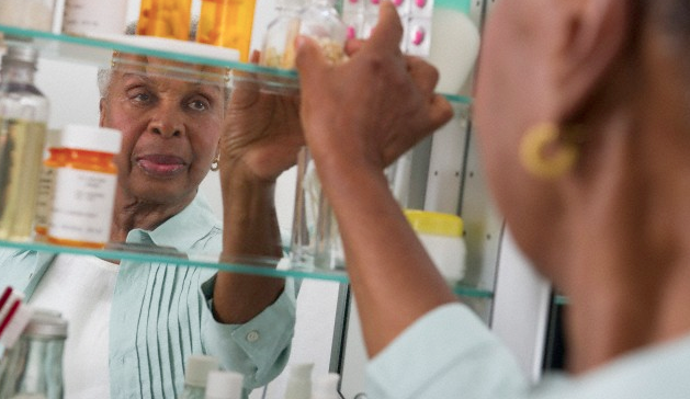 A senior woman reaching into her medicine cabinet for a prescription bottle