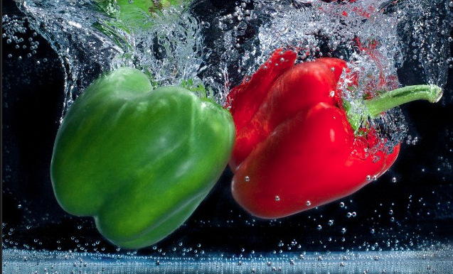 A green and a red bell pepper submerged in water