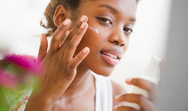 A woman holding a sunscreen bottle as she applies it to her face