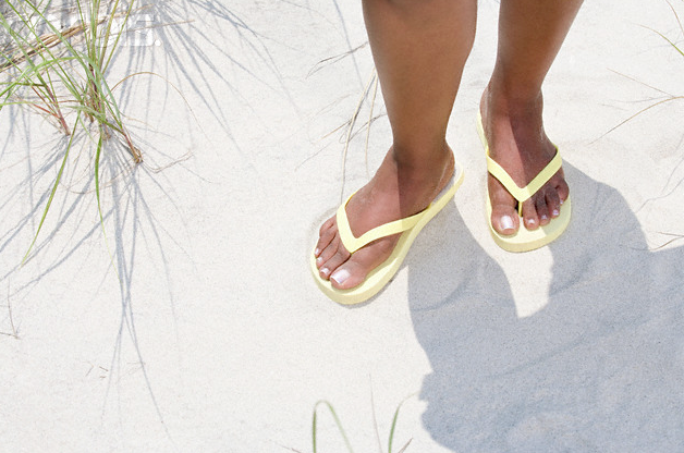 A woman's feet wearing yellow flip flops in the sand