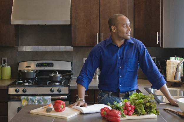 A man standing at his kitchen counter, with fresh vegetables on top of it