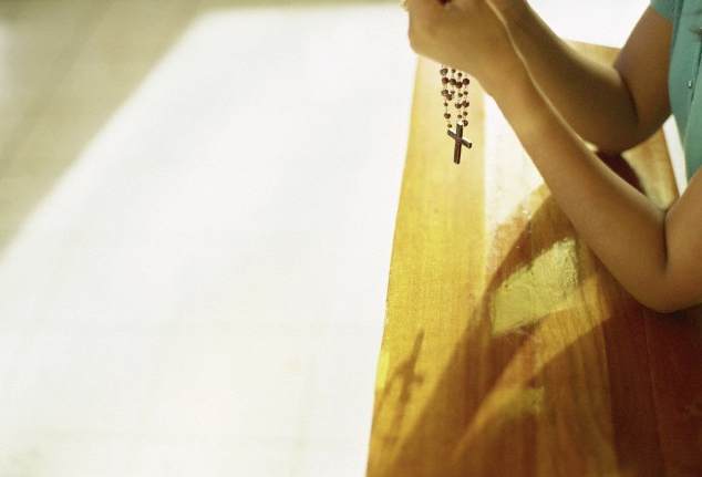 A woman kneeling at church holding rosary
