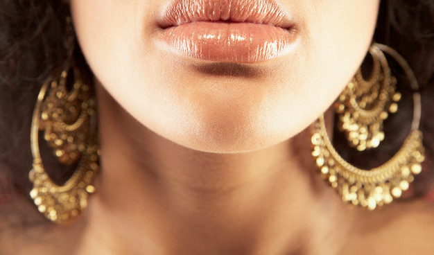 A close-up of a woman with gold earrings wearing nude lipstick