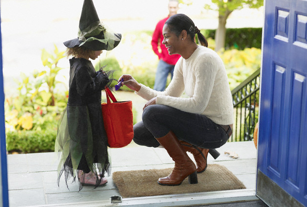 A woman kneeling down and giving candy to a little girl for Halloween