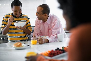 A teenager eating in the kitchen with his parents