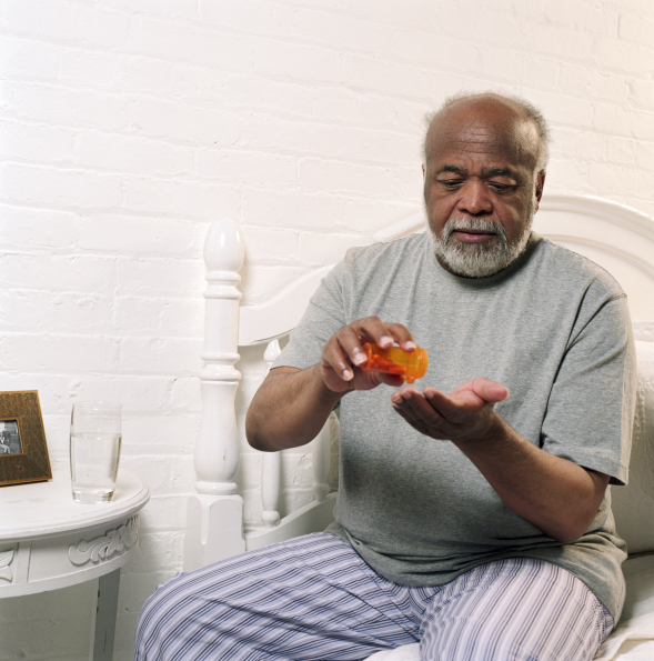 older african american man pouring pills from a prescription bottle into his hand