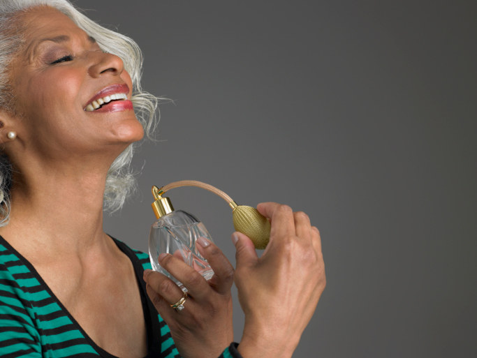 older woman spraying perfume on neck and smiling