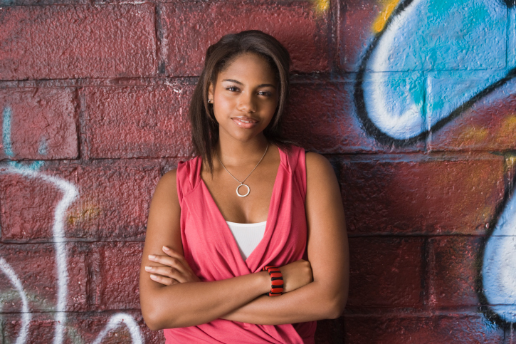 teen standing, leaning against wall arms crossed