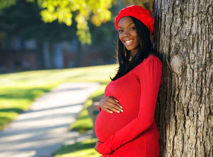 pregnant woman posing outside leaning against a tree