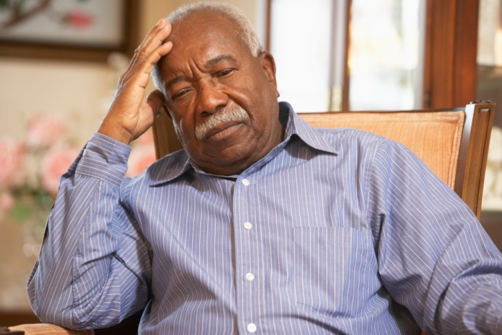 senior man sitting in chair, with hand on head