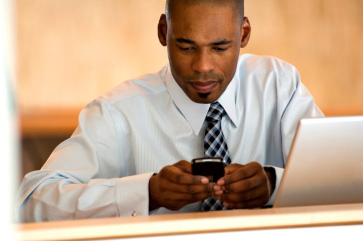 African American Black businessman texting and with laptop