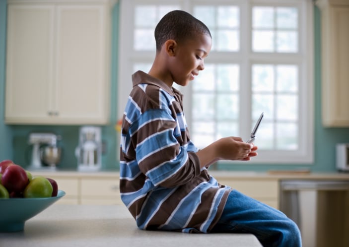 young African American boy sitting in kitchen looking at cell phone