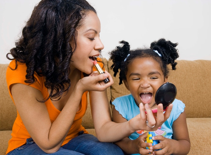 African american mother and daughter putting on lipstick makeup