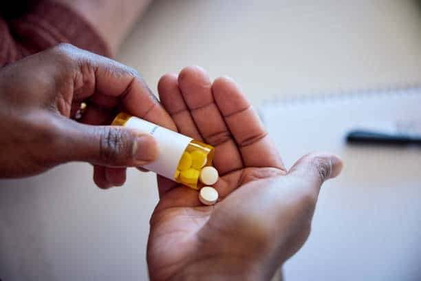 A person's hands dispensing white pills from a yellow prescription bottle into their palm.