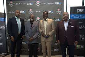 Four Black men in business attire stand smiling in front of a dark banner with 'ZER' logos, one holding a small award.