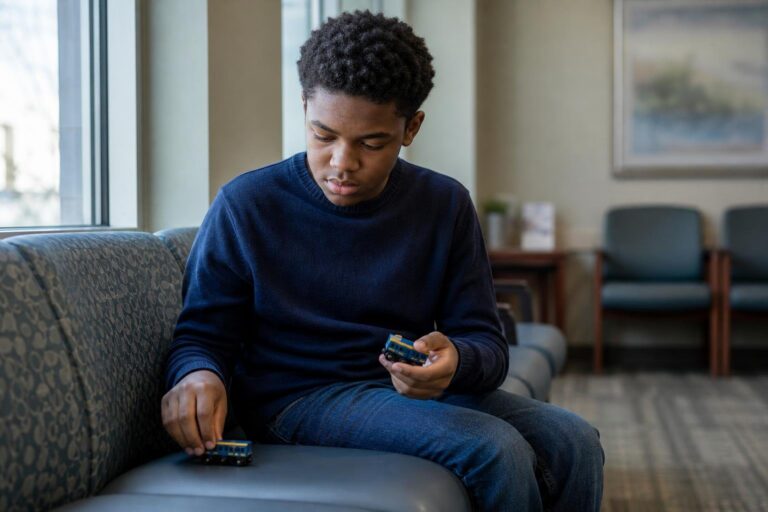 Black teen with Asperger's syndrome holds model trains in a quiet clinic waiting area.
