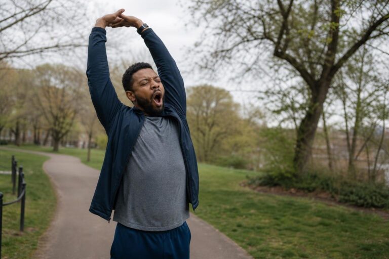 Black man yawning and stretching on a park path while practicing easy health tricks.