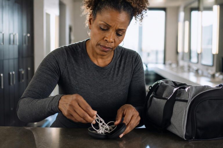 Woman organizing tangled earbuds at a gym counter to solve common gym problems.